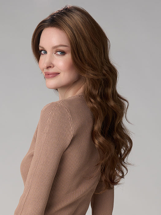 Woman with long wavy hair wearing a beige sweater against a gray background