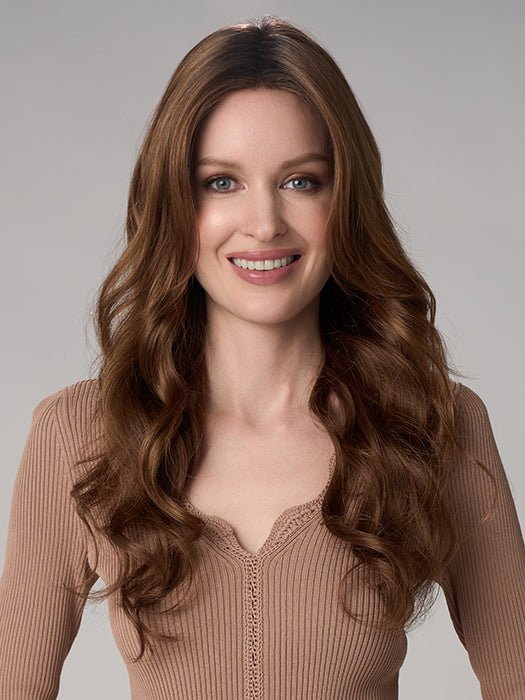 Woman with long wavy brown hair wearing a beige top against a gray background