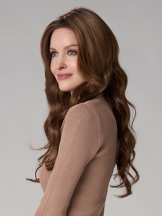 Woman with long, wavy brown hair wearing a beige sweater against a plain background