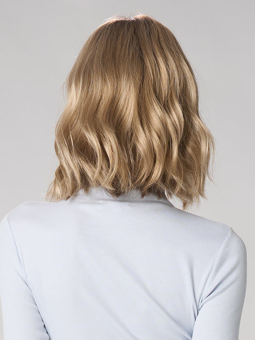 Person with wavy blonde hair wearing a light gray top against a plain background