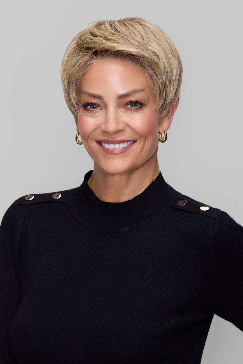 Woman with short blonde hair wearing a black top with gold buttons on a gray background