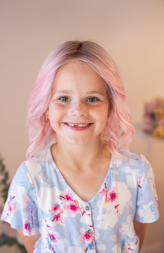 Young girl with pink hair wearing a floral shirt indoors.
