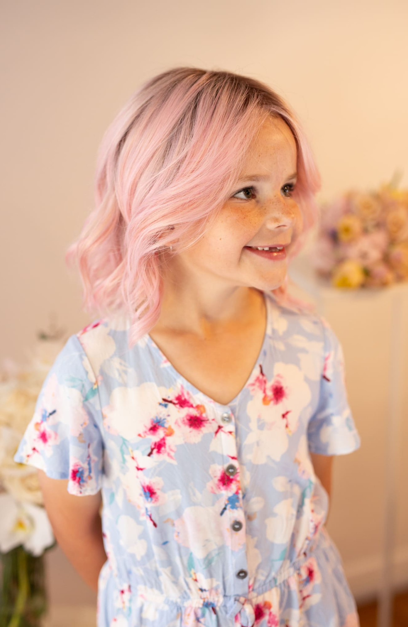 Child with pink hair wearing a floral dress in a softly lit room.