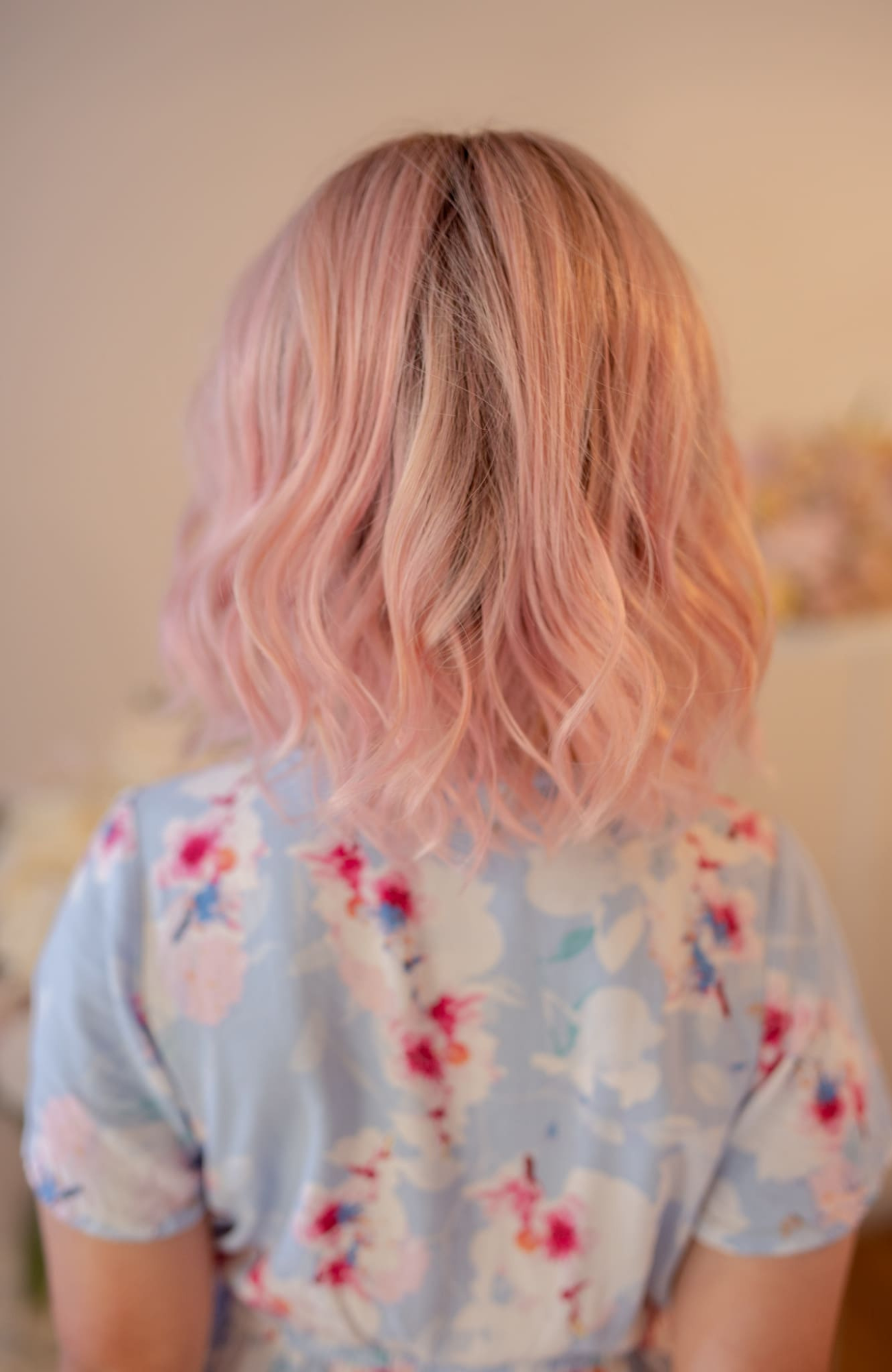 Person with pink hair wearing a floral shirt in a neutral setting