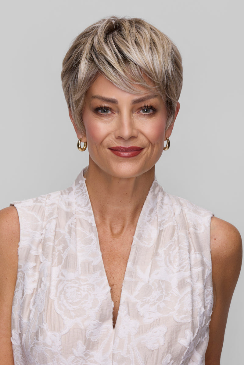 Woman with styled hair wearing a white sleeveless top against a plain background